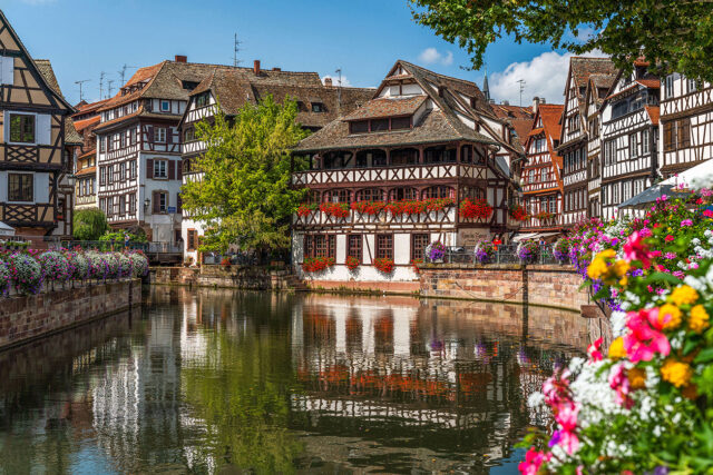 Buildings adorned with flowers, reflecting in the river